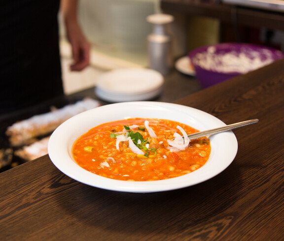 Eine warme Cremesuppe mit einem Löffel darin steht auf einem hölzernen Untergrund. 