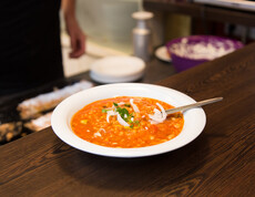 Eine warme Cremesuppe mit einem Löffel darin steht auf einem hölzernen Untergrund. 