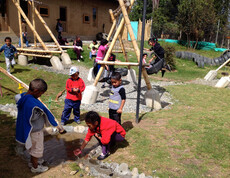 Ein Spielplatz im Freien, auf dem zahlreiche Kinder spielen. Manche sind beim Schaukeln, andere spielen mit dem Wasser. 