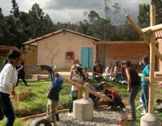 Viele Kinder, die im Freien spielen. Schauplatz ist ein Spielplatz. Im Hintergrund sitzen einige Mütter mit ihren Kindern.