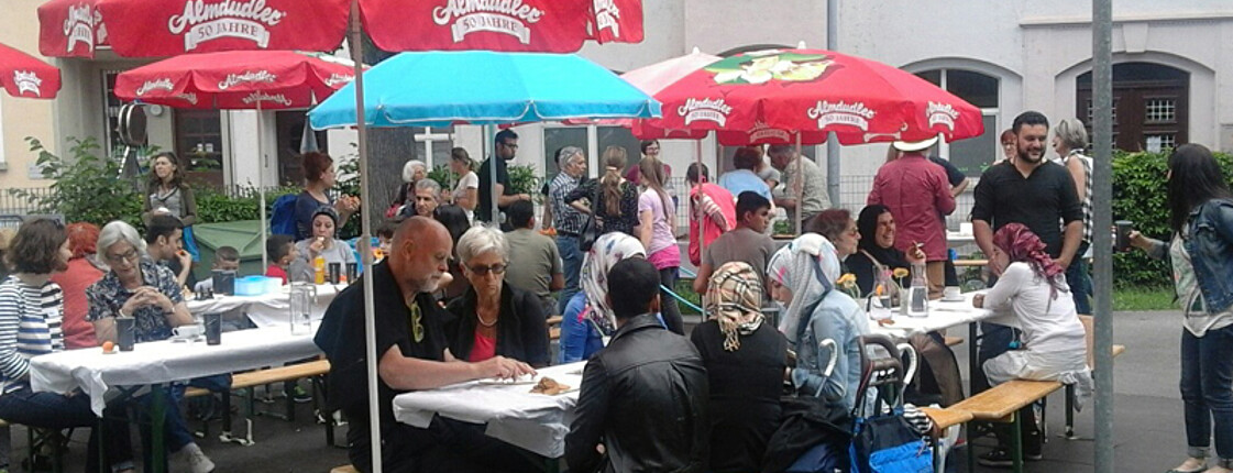 Eine Feier im Freien mit vielen Menschen. Sie sitzen auf Holzbänken und essen.