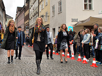 Eine Modenschau, mitten in einer Stadt. Frauen und Männer präsentieren ihre Kleidung.