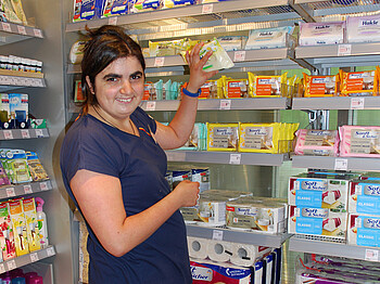 Bianca Panek, eine junge erwachsene Frau mit schwarzen langen Haaren und einem dunkelblauen t-Shirt, ist gerade am Einräumen von Waaren in einem Drogeriemarkt. 