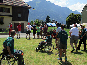 Mehrere Klienten der Werkstätten spielen auf einem grünen Rasen Fußball. Zwei von Ihnen sitzen dabei in ihrem Rollstuhl.