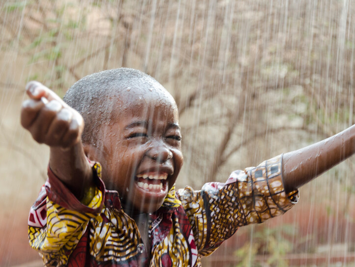 Little,Native,African,Boy,Standing,Outdoors,Under,The,Rain,(water