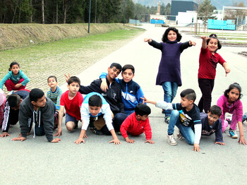 Viele Flüchtlingskinder versammeln sich im Freien für ein Lauftraining. Sie tragen Sportkleidung und sind schon in Startposition.