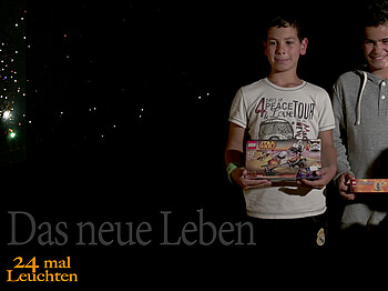 Zwei junge Buben erleuchtet auf schwarzem Hintergrund. Die Kinder strahlen und halten ein Geschenk in der Hand. 