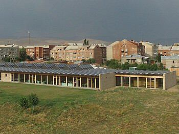 Eine Luftaufnahme zeigt das Haus Emils auf einer großen Wiese. Dahinter sind Wohnblöcke und Berge.