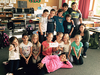 Die 3b Klasse der Volksschule Rankweil-Brederis steht mit Caritasmitarbeiterin Sabine Längle zu einem Gruppenfoto zusammen. Die Mädchen sind in der forderen, die Buben stehen in der Reihe. Der Hintergrund ziert ein gewöhnliches Klassenzimmer. 