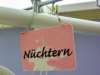 Ein kleines rosa Schild mit der Aufschrift "Nüchtern". Das Schild wurde mit einer dünnen Kette an einer Stange befestigt