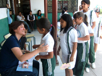 Eine Frau sitzt auf einem Stuhl und begrüßt herzlich die Schülerinnen von Ecuador. Die Kinder tragen alle eine Schuluniform und stehen in einer Reihe.