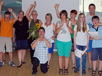 Menschen mit Beeinträchtigung und Betreuer stehen für ein großes Gruppenbild zusammen. Einige strecken ihre Arme dabei hoch. Der großteil ist weiß bekleidet. 