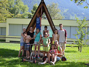 Kinder und Jugendliche stehen im Freien für ein Gruppenfoto zusammen. Sie befinden sich in einer Wiese, vor einem kleinen Holzhaus. 